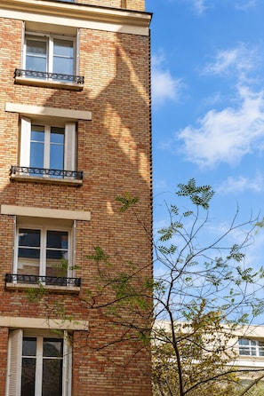 A multi-story building with brick facade, multiple windows with shutters, and a clear sky. - New Listing (Paris)