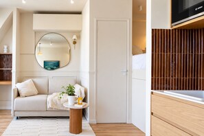 Ein modernes Zimmer mit einer Couch, einem runden Spiegel, einem kleinen Tisch mit Pflanze und einem Fernseher auf einem Holzständer.
