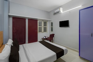 A hotel room with a bed, a desk, a chair, a wardrobe, and an air conditioning unit. - Super Hotel O Mallapur Crossway (Hyderabad)
