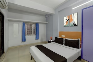 A hotel room with a bed, a window with blue curtains, a wall-mounted artwork, and a bedside table with a vase of flowers. - Super Hotel O Mallapur Crossway (Hyderabad)