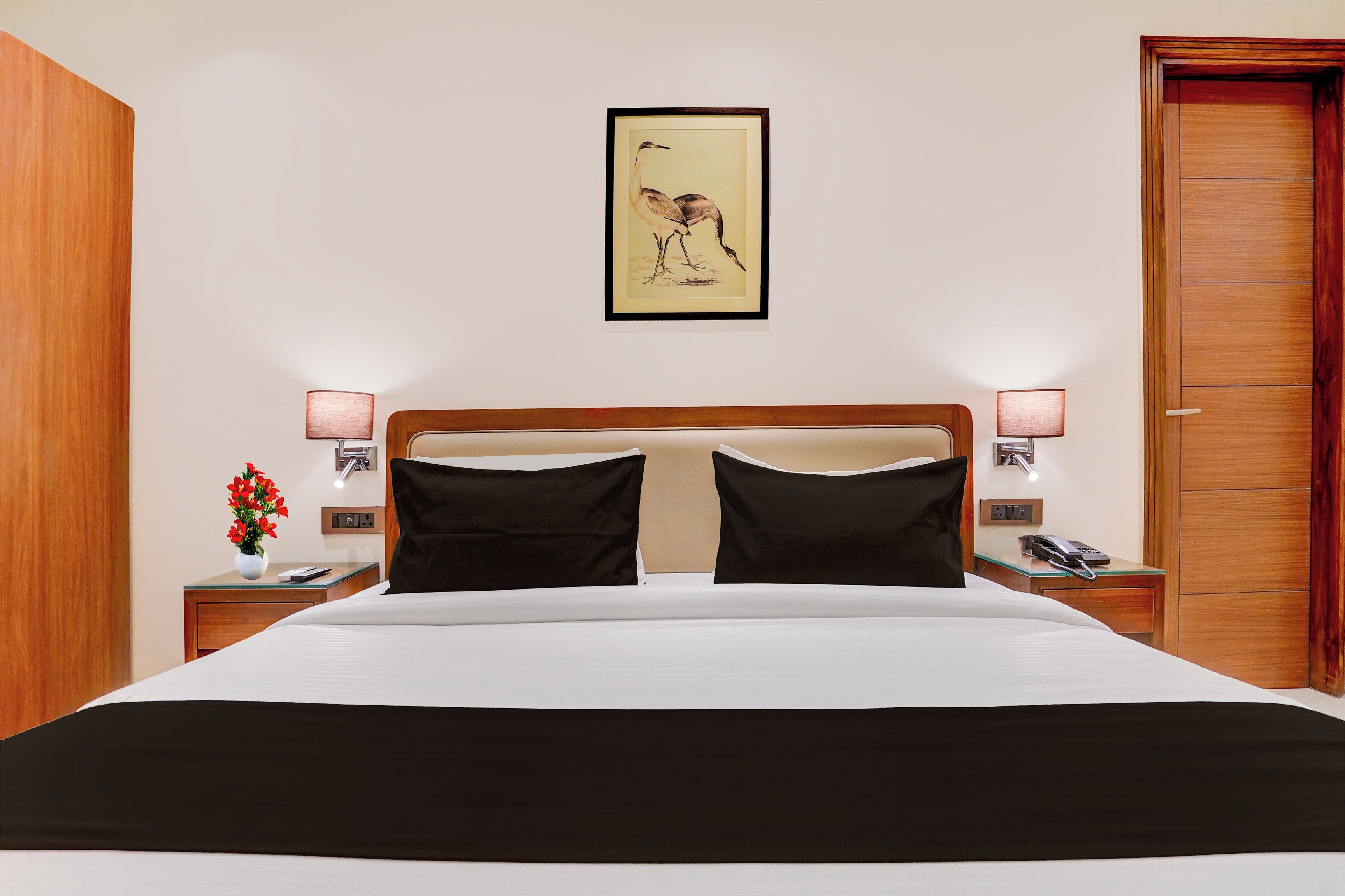 A hotel room with a bed, two bedside lamps, a telephone, a vase with flowers, and a framed picture on the wall.