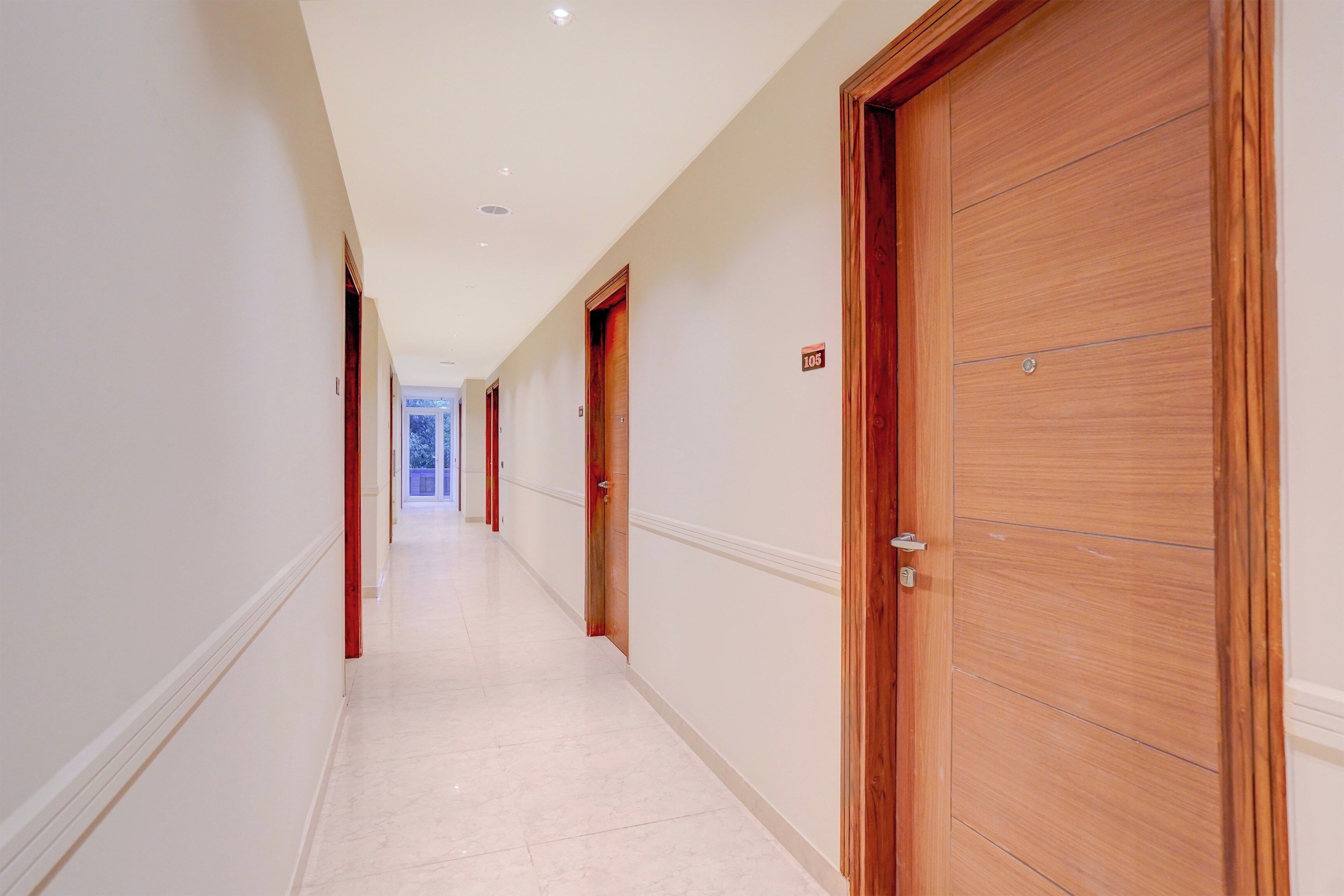 A hotel corridor with wooden doors, white walls, and a tiled floor.