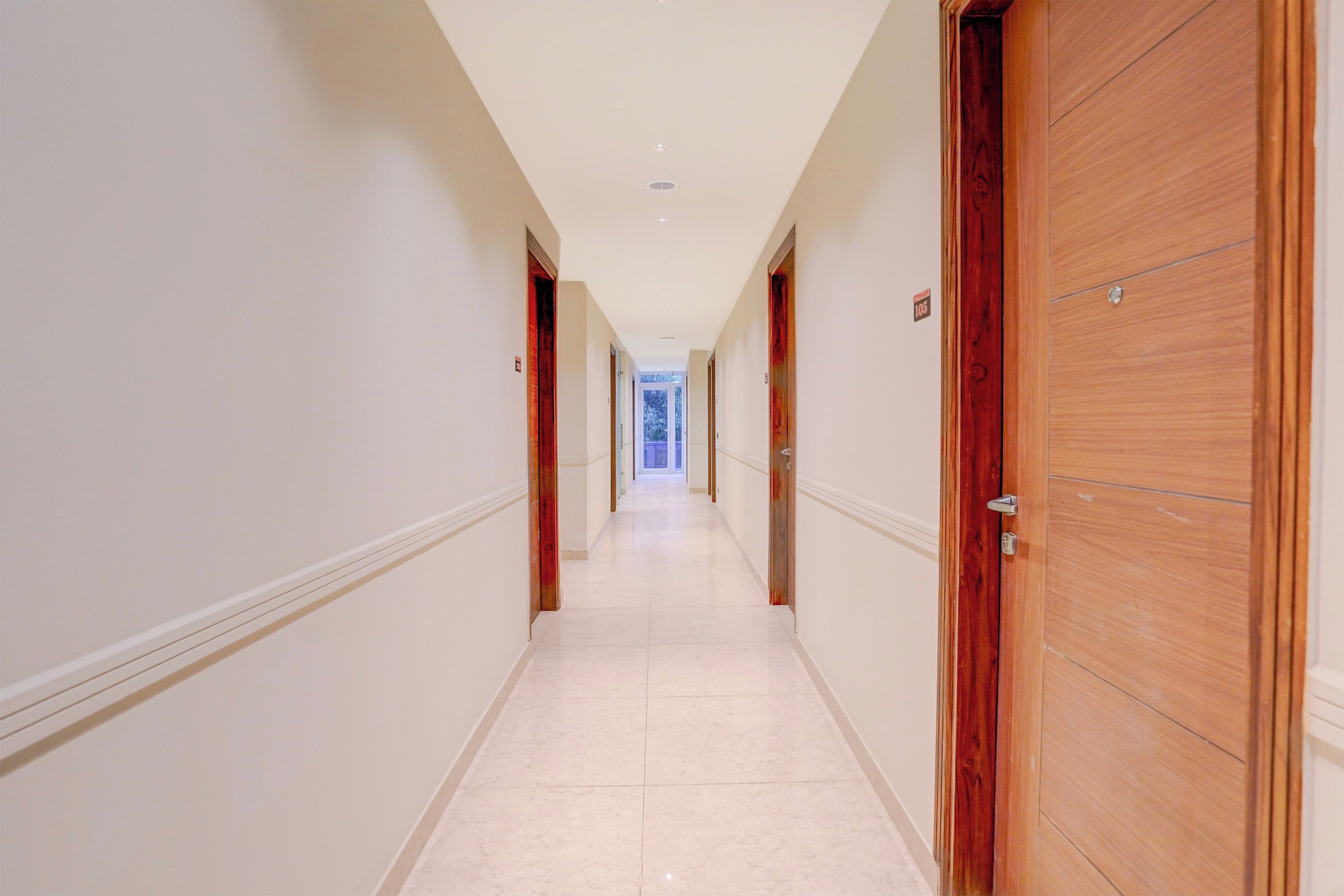 Un pasillo de hotel con puertas de madera, paredes blancas y suelo de baldosas.