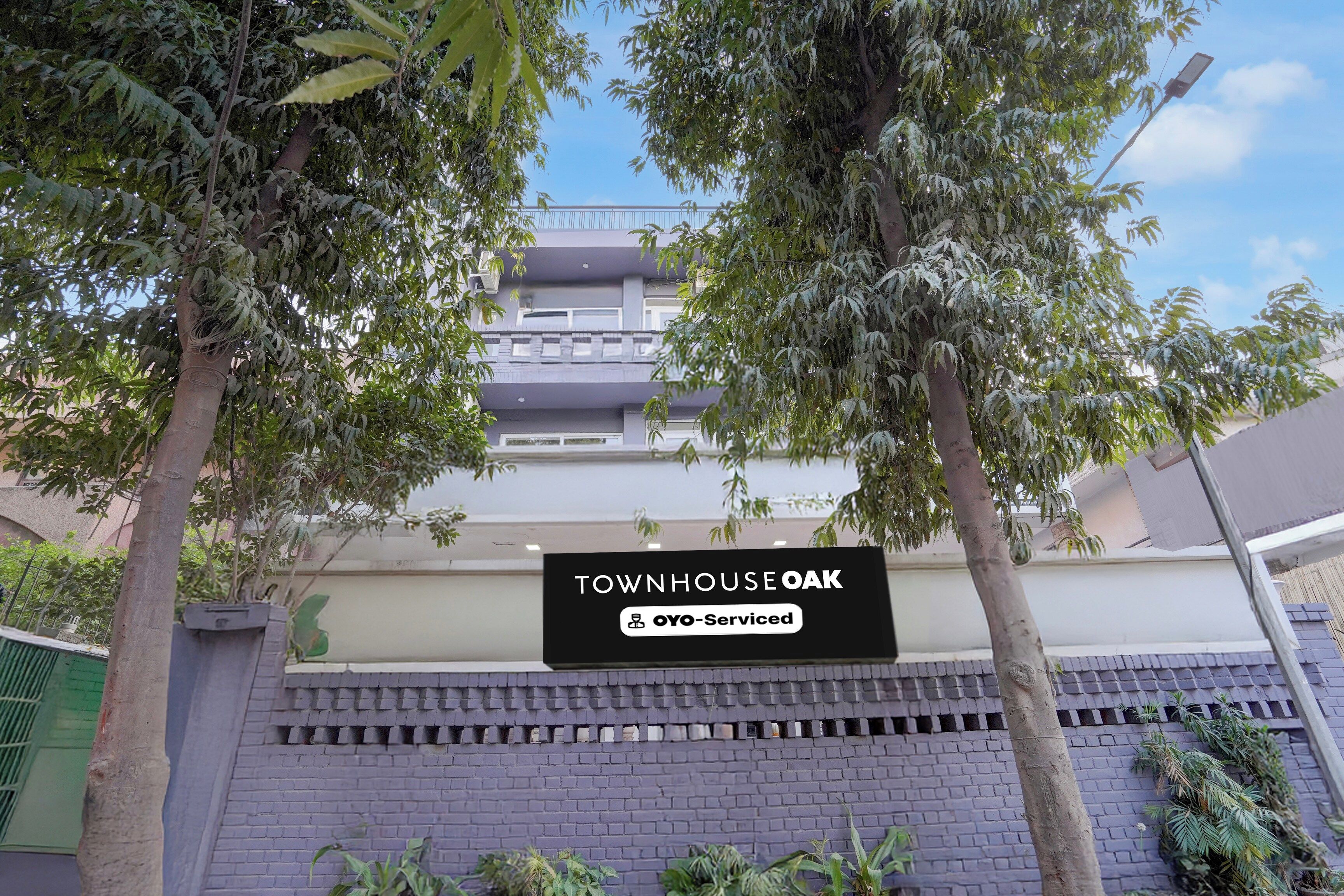 Un edificio residencial con un letrero que indica 'TOWNHOUSE OAK' y servicios 'OYO-Serviced'.