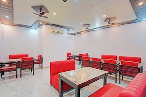 Un restaurante con cabinas tapizadas de rojo y mesas, un techo blanco con iluminación empotrada y un equipo de aire acondicionado.