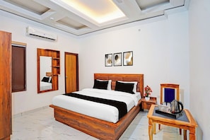 Habitación de hotel con una cama grande, un armario de madera, una mesita de noche con cafetera y un espejo.