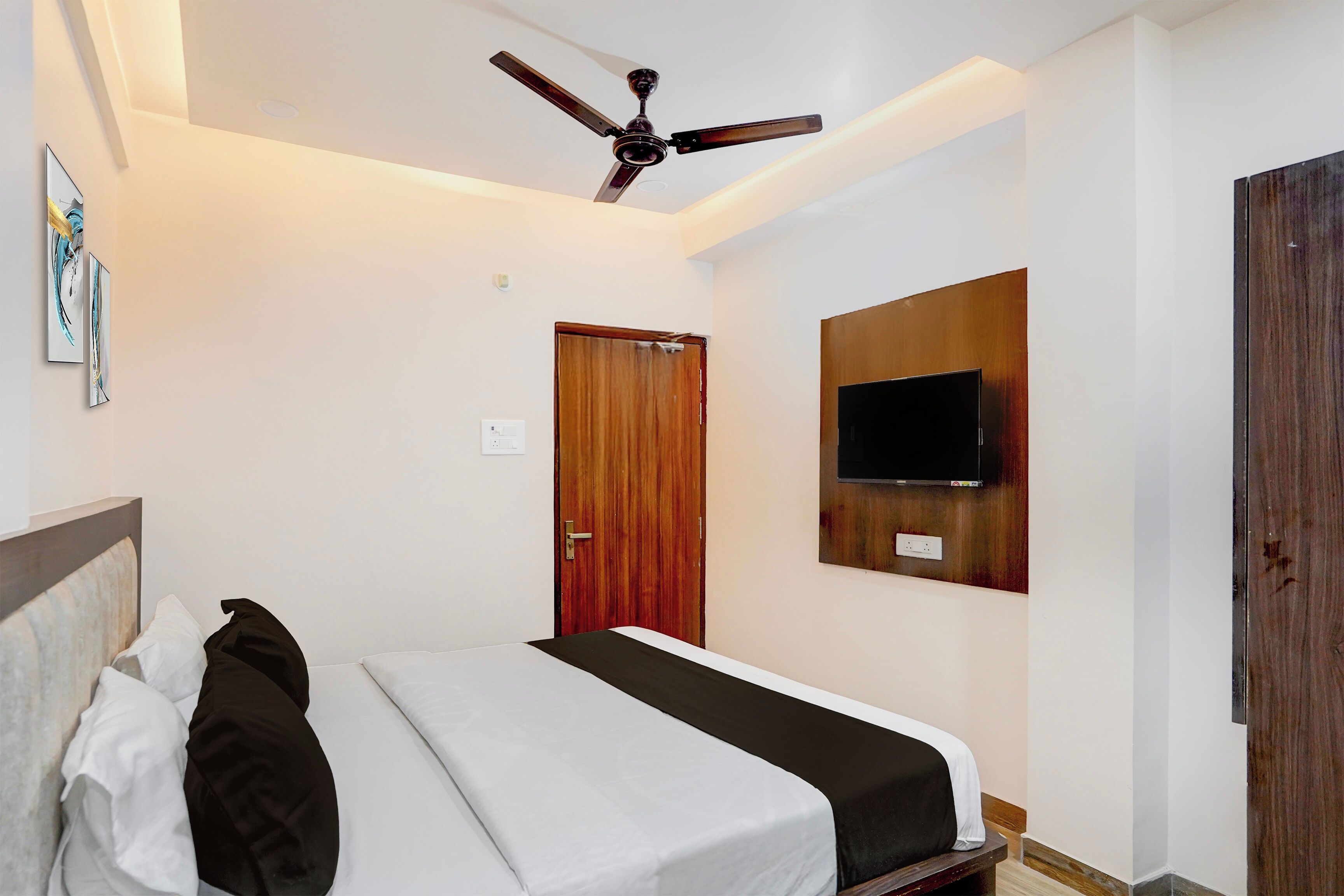A bedroom with a bed, a ceiling fan, a wooden door, and a mounted television.