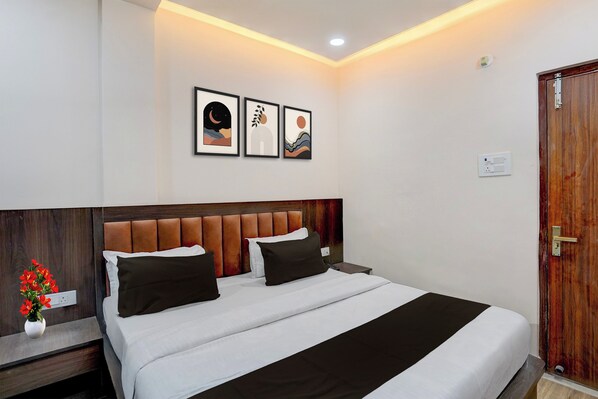 Quarto de hotel com cama, mesa de cabeceira, vaso com flores e três quadros na parede.