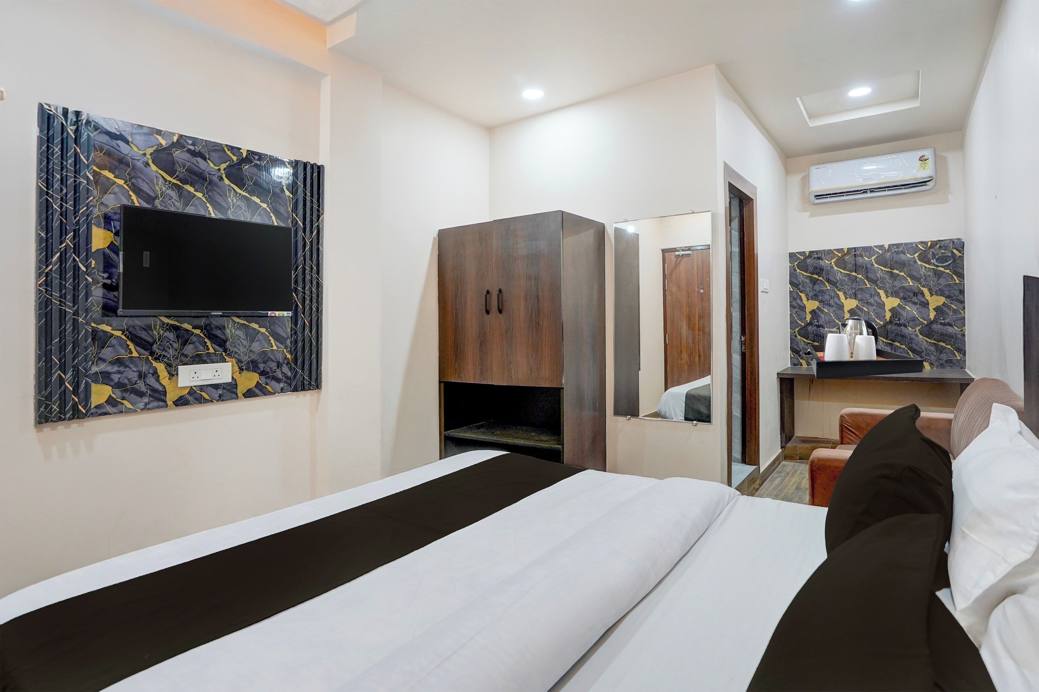 Una habitación de hotel con una cama, un armario, un televisor montado en la pared y un baño visible a través de una puerta abierta.