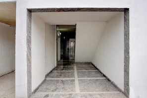 Um corredor estreito, com piso escuro, paredes brancas e azulejos, que leva a uma porta no final.