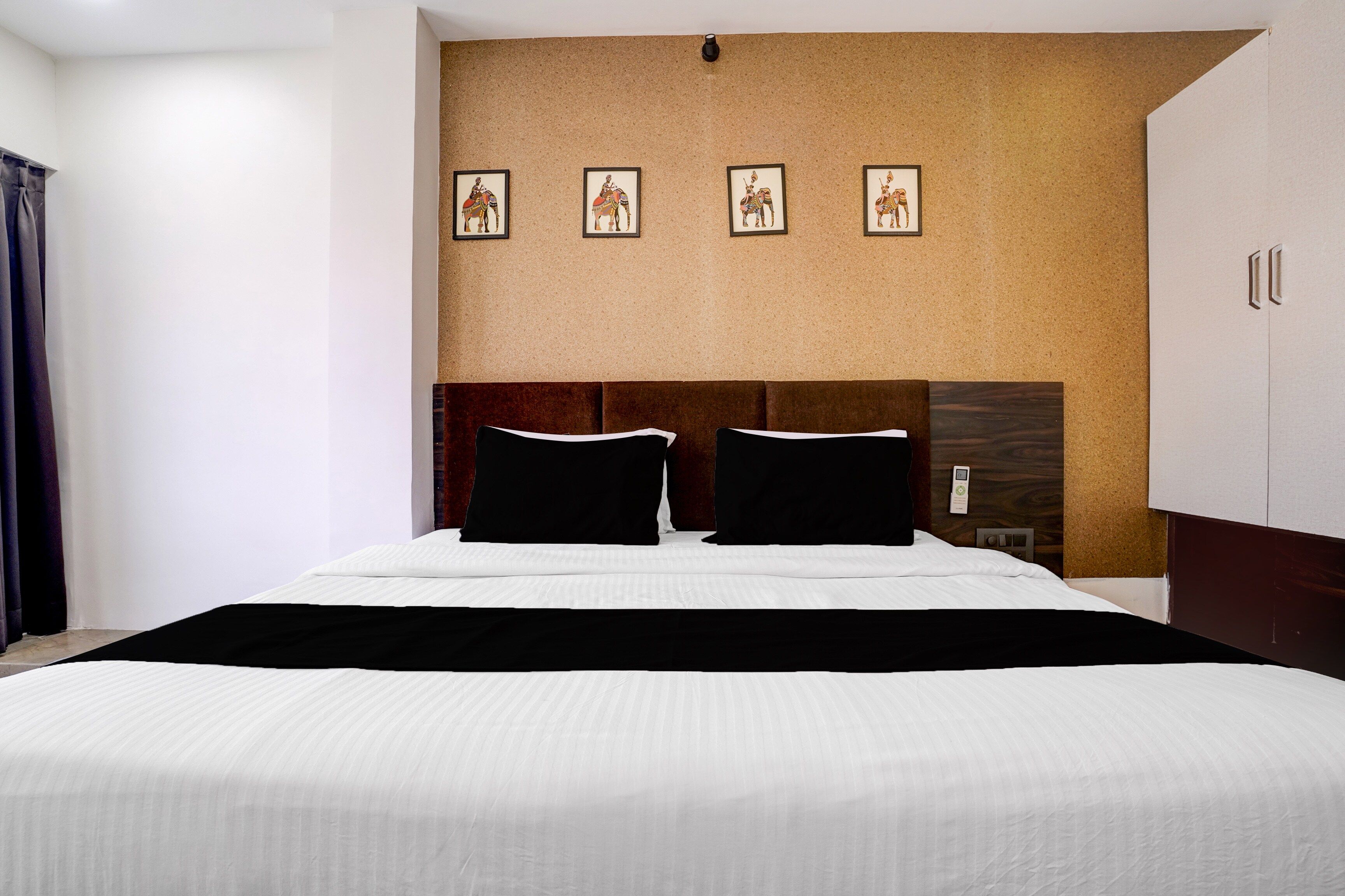 Habitación de hotel con una cama grande, cabecero de madera, pared cubierta de corcho con fotografías enmarcadas y un armario.