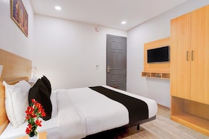 A hotel room with a bed, a TV mounted on the wall, a wooden wardrobe, and a door. - Super OYO Townhouse Deva Road Lucknow (Lucknow)