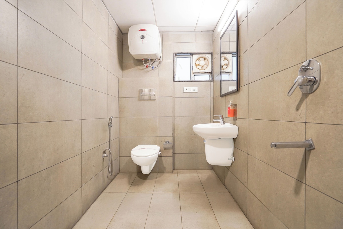 Un baño pequeño con azulejos, que incluye un inodoro, un lavamanos, un secamanos y un espejo.