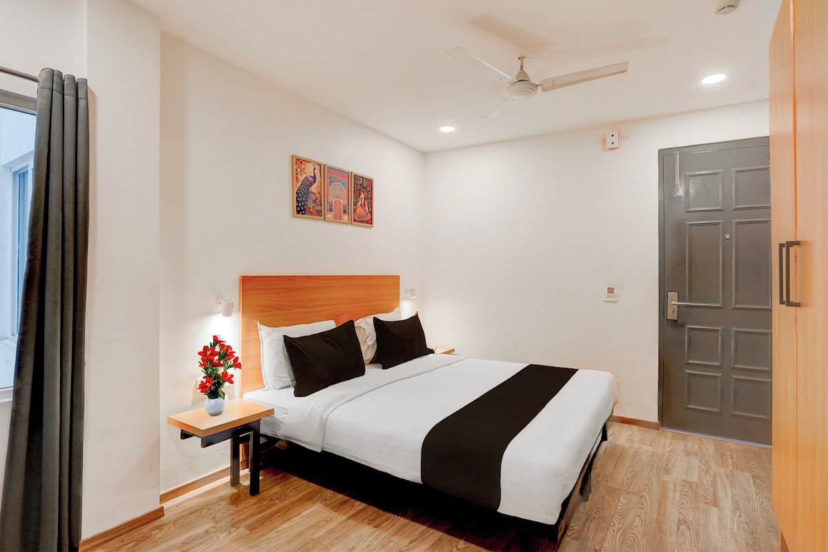 Una habitación de hotel con cama, mesita de noche, lámpara, una obra de arte y una puerta.