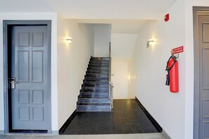 Una escalera que lleva a un piso superior, un extintor fijado en la pared y una puerta con una placa de número.