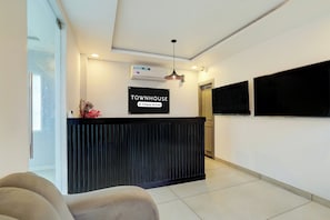 Un área de recepción con un mostrador negro, un cartel que indica servicio de empresa, un aire acondicionado instalado y un televisor de pared.