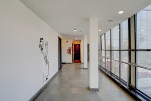 A corridor with a fire extinguisher mounted on the wall, a door at the end, and large windows on the right side. - Super OYO Townhouse Deva Road Lucknow (Lucknow)