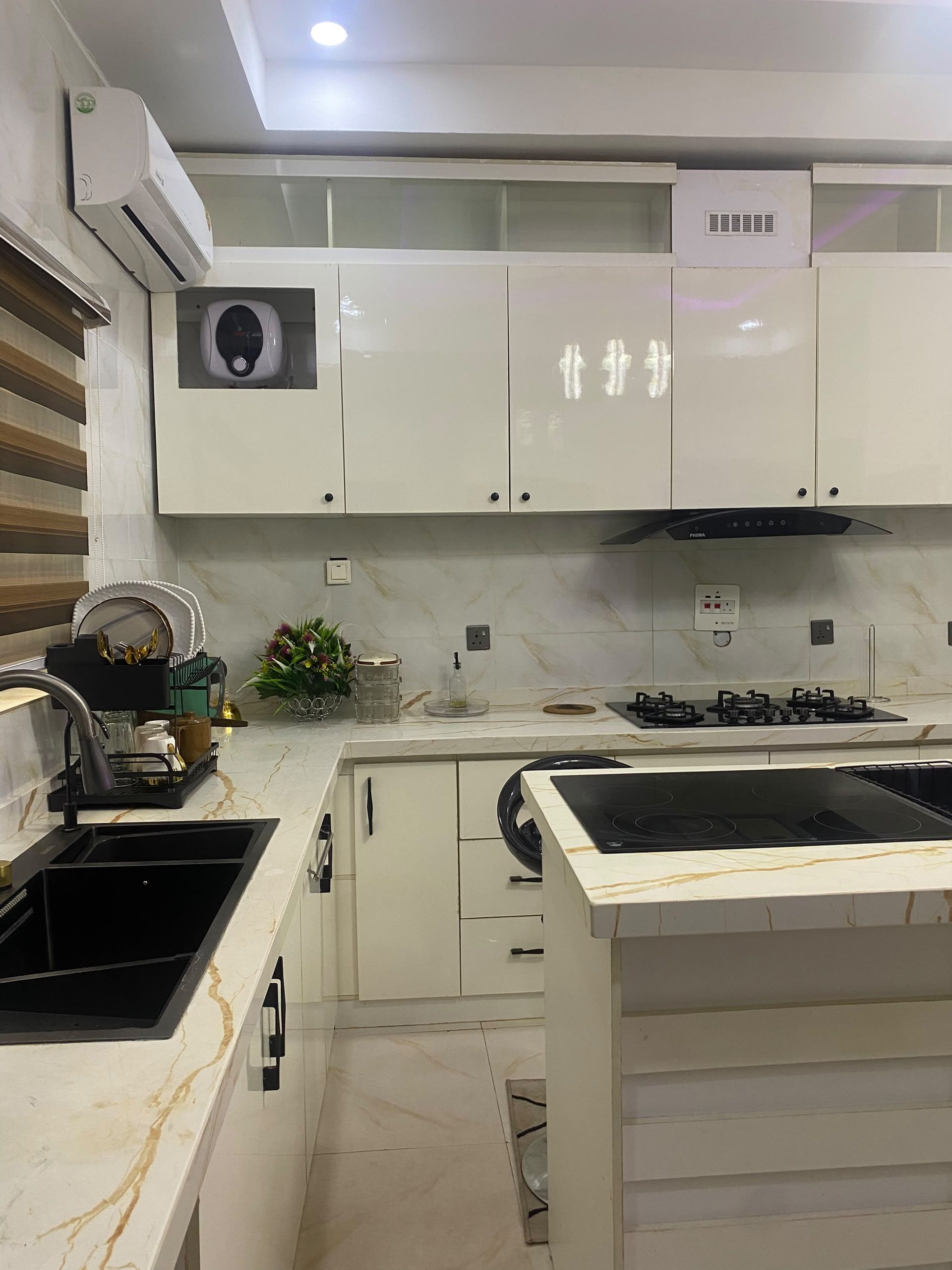 Una cucina moderna con mobili bianchi, piano cottura integrato e un'isola in marmo.