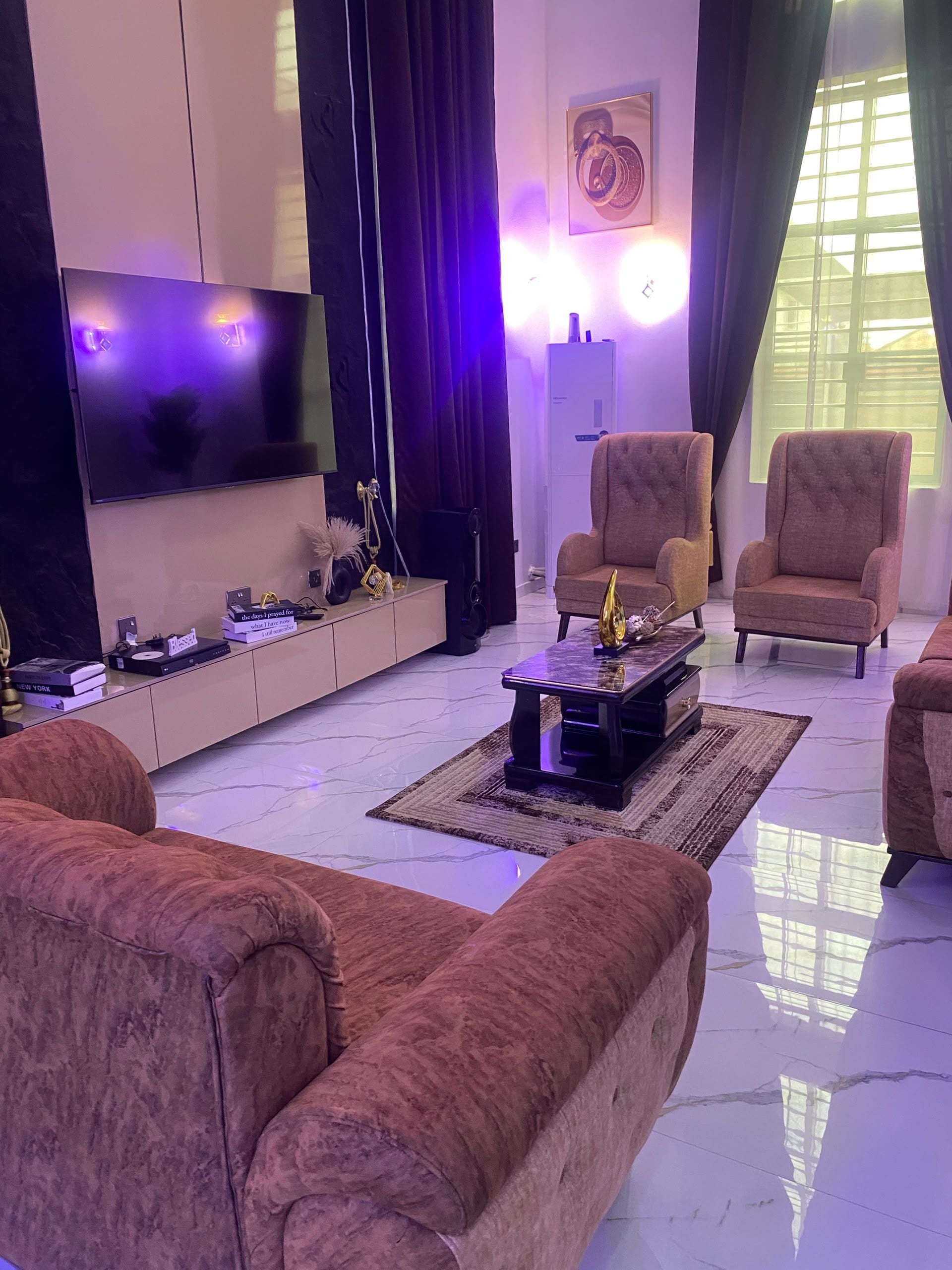 A modern living room with a flat-screen TV, two armchairs, a coffee table, and a patterned rug.