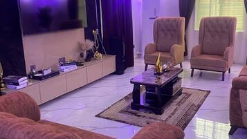 A modern living room with a flat-screen TV, two armchairs, a coffee table, and a patterned rug.