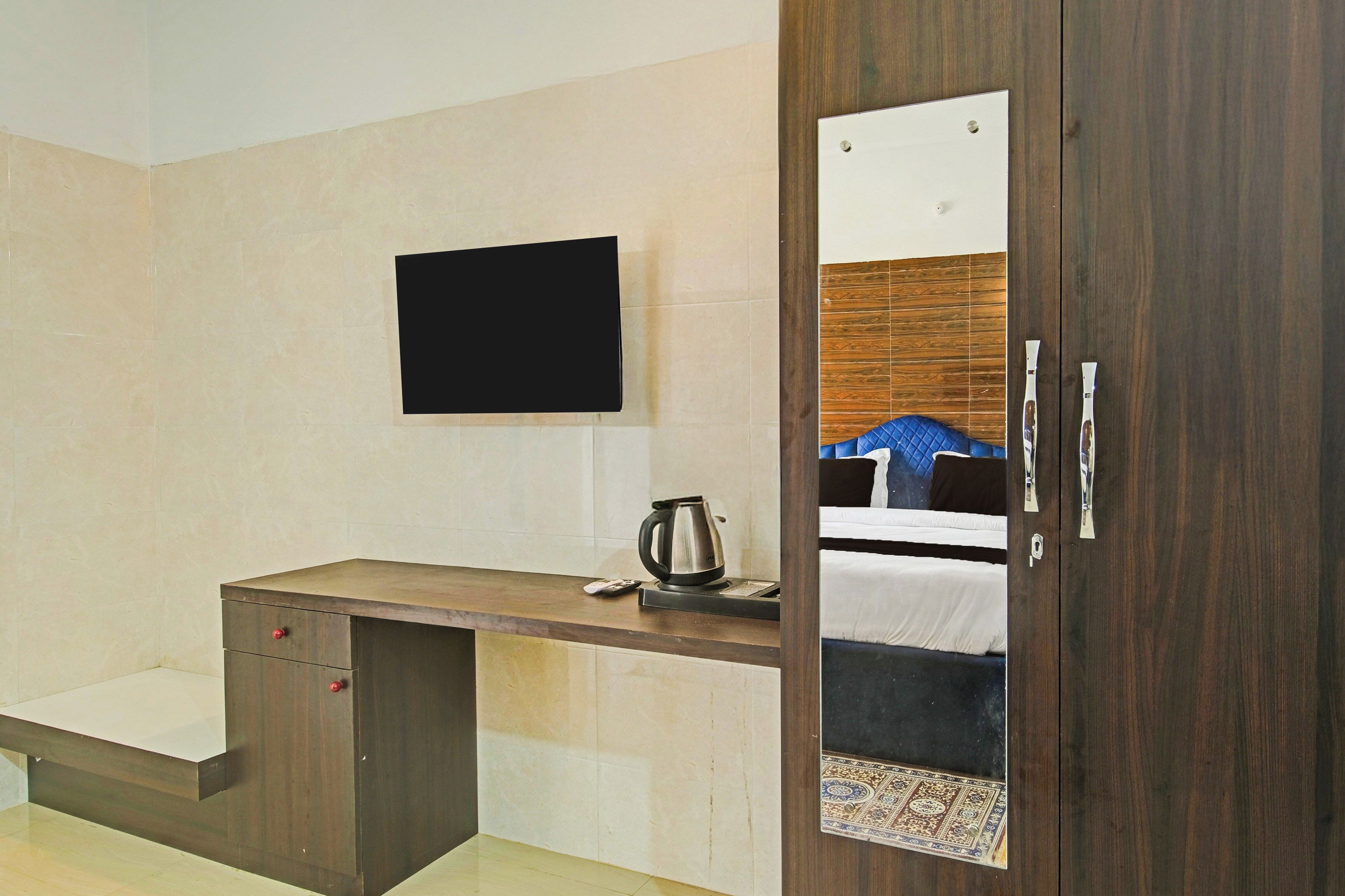 Hotelkamer met een houten bureau, een flatscreen televisie aan de muur, een koffiezetapparaat en een bed met een kamerkleed met dessin.