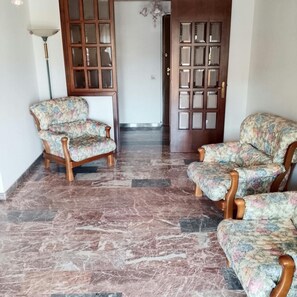 Habitació amb sòl de marbre, dues butaques amb motius florals, una porta de fusta amb panells de vidre i una làmpada de peu.