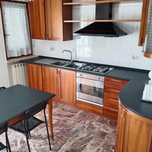 Una cucina con mobili in legno, un piano cottura in acciaio inossidabile, un lavello e una finestra con tenda.