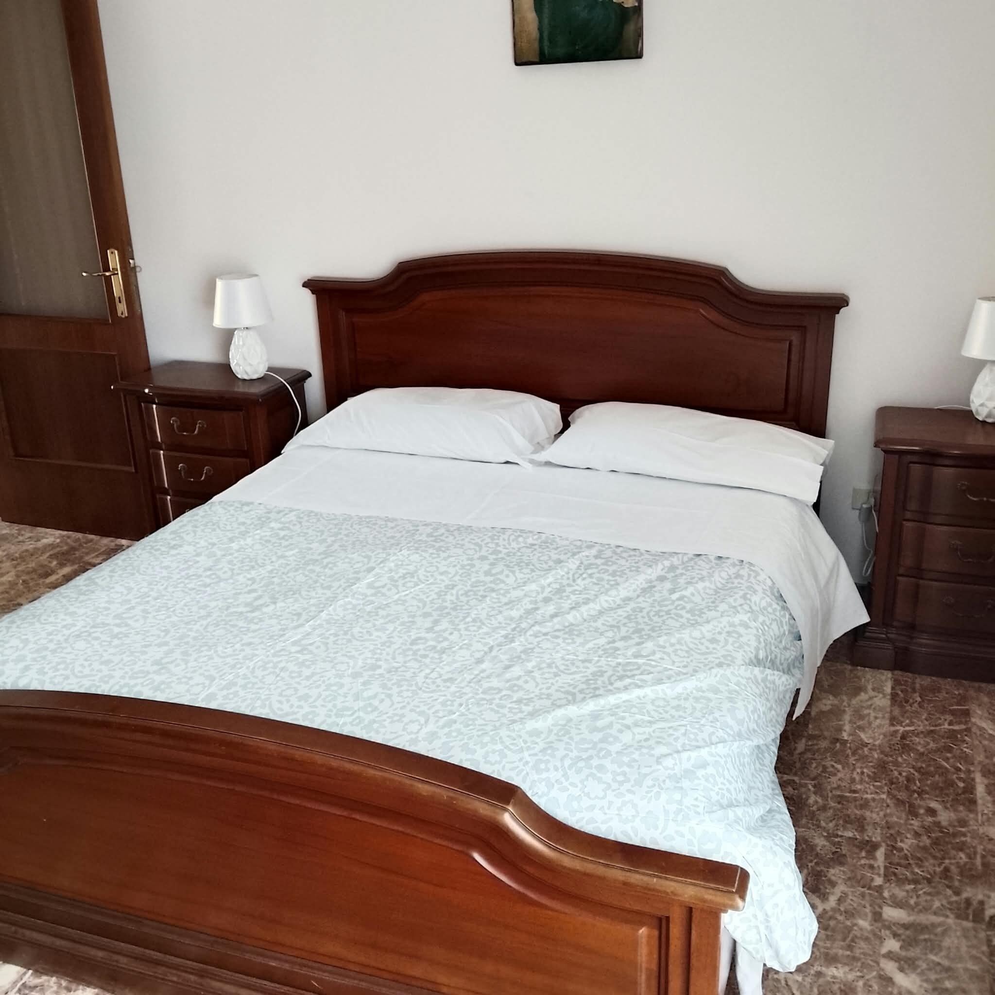 Un lit en bois avec une tête de lit, deux tables de chevet avec des lampes et une couvre-lit à motifs.