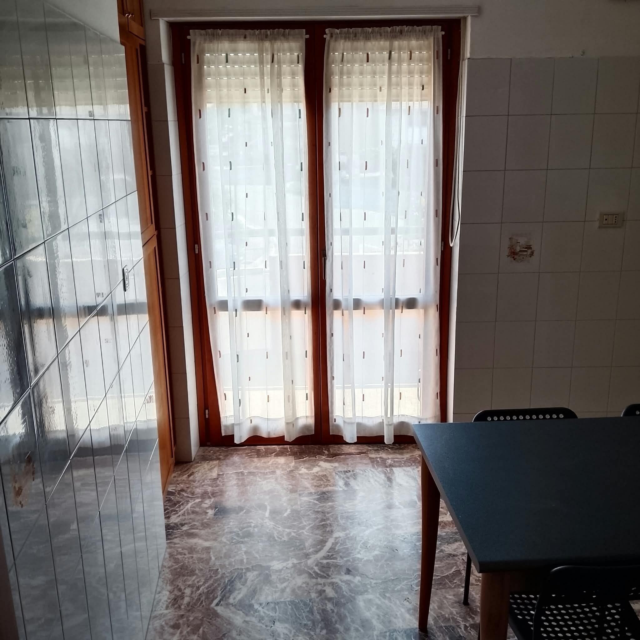 Une pièce avec un sol carrelé, une table et une fenêtre avec des rideaux.