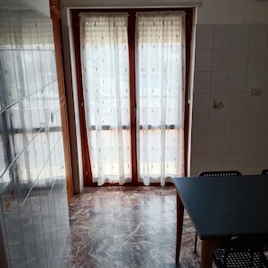Una stanza con pavimento piastrellato, un tavolo e una finestra con tende.