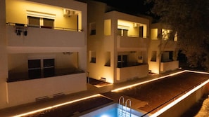A modern multi-story building with a swimming pool and outdoor lighting. - Deppie First Floor - Miralis Apartments (Episkopos)