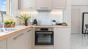 A modern kitchen with a built-in oven, a coffee maker, and a plant on the counter. - Maria Ground Floor - Miralis Apartments (Episkopos)