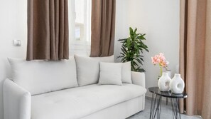 A white sofa with two pillows, a potted plant, and two white vases on a small round table. - Maria Ground Floor - Miralis Apartments (Episkopos)