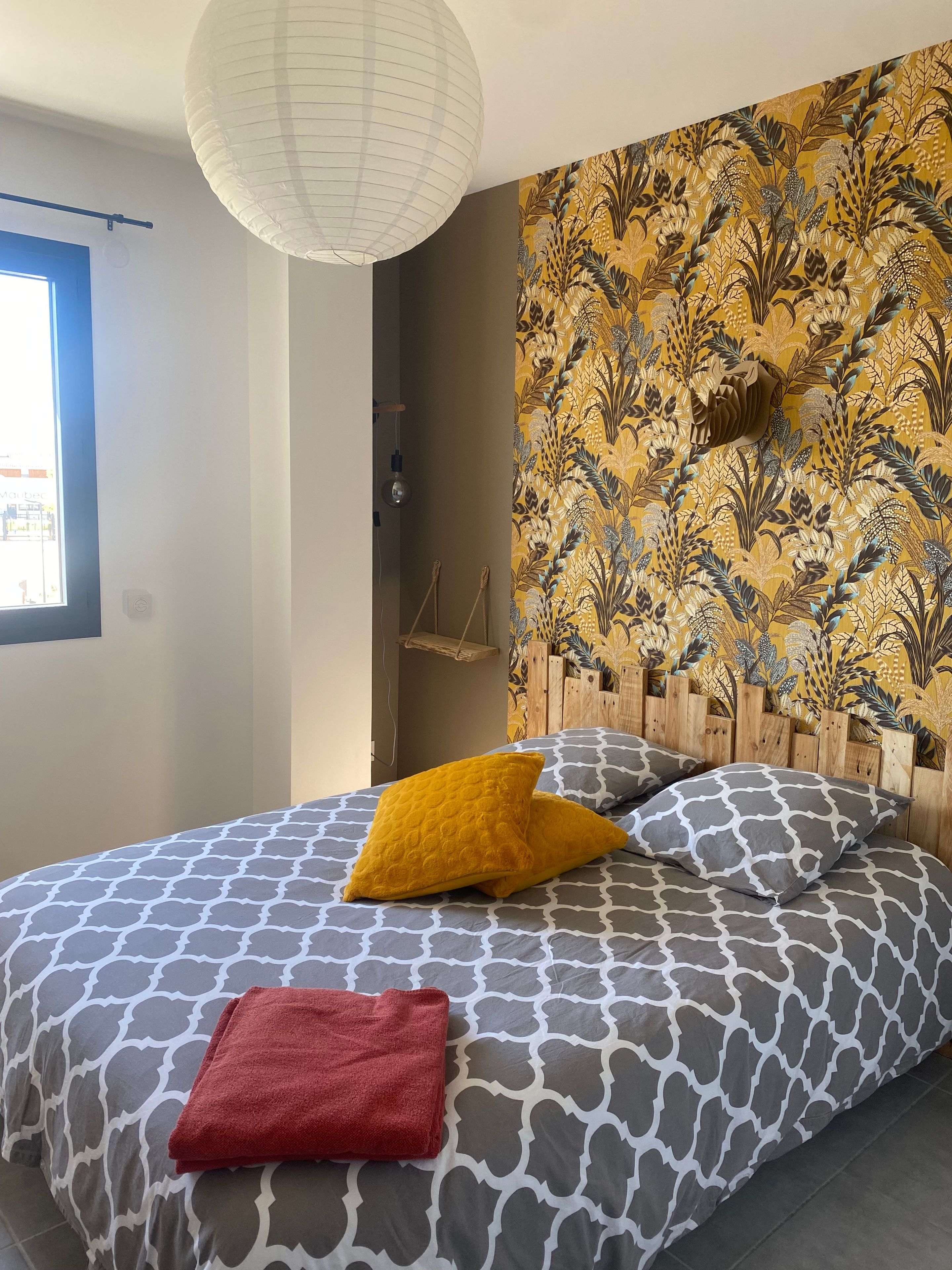 Een bed met beddengoed met een patroon, een rode handdoek en een muur met botanische behang.