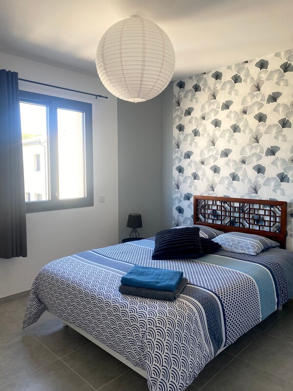 Une chambre à coucher avec un lit, une table de chevet, une lampe et une fenêtre avec des rideaux.