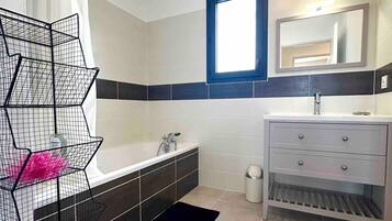 Een badkamer met een badkuip, een wastafel, een spiegel en een zwart metalen plankje.