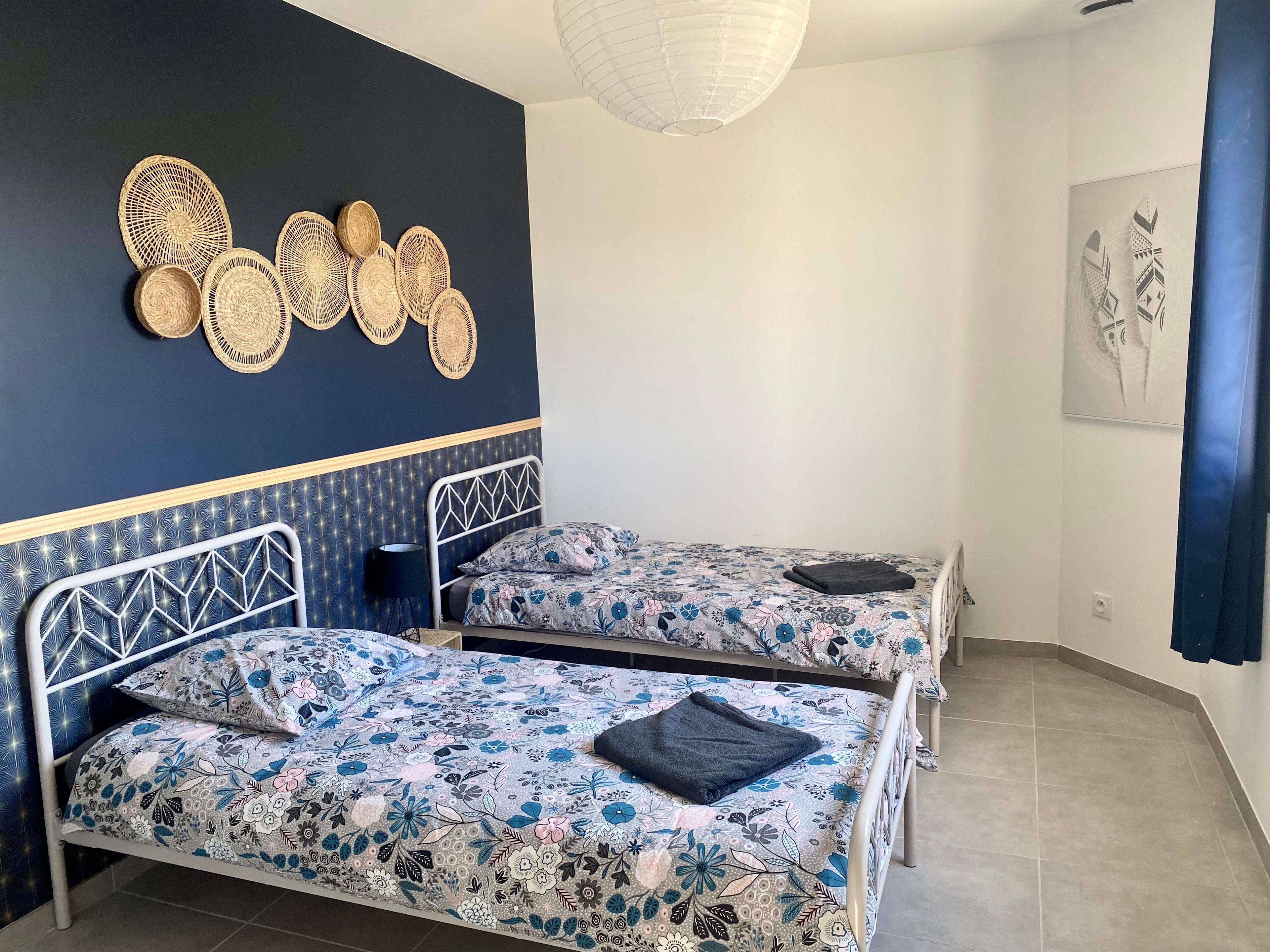 A room with two beds, a wall-mounted light fixture, and a ceiling fan.