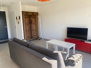 Ett vardagsrum med en soffa, en tv på ett rött tv-bord, ett vitt bord och en trädörr.