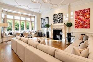 A spacious living room with a large beige sofa, a fireplace, and artwork on the walls. - Grand Knightsbridge Home High Ceilings Easy Access (London)