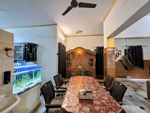 Een kamer met een eettafel, stoelen, een plafondventilator, een aquarium en een houten kast met spiegel.