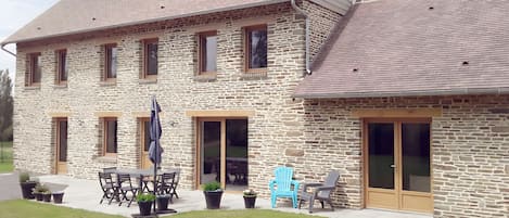 A stone house with a large patio, outdoor seating, and a covered area.
