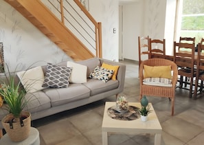 A living room with a grey sofa, a wicker chair, a coffee table, and a staircase.