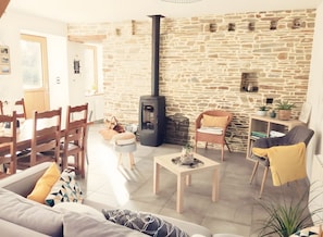 A cozy living room with a stone wall, a fireplace, a dining area with wooden furniture, and a comfortable seating arrangement.