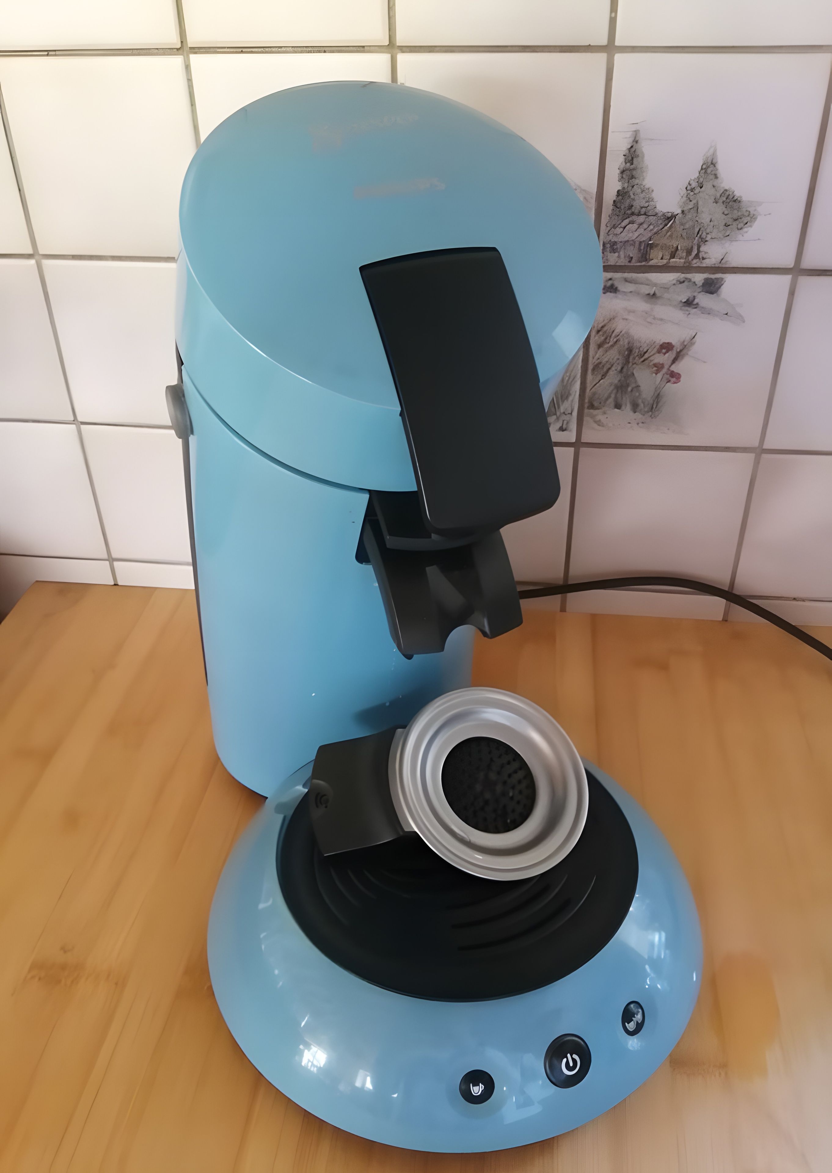 Une machine à café bleue, dotée d’un panneau de commande noir et d’un bac d’égouttement amovible, posée sur une surface en bois.