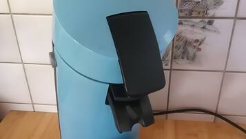 Eine blaue Kaffeemaschine mit schwarzem Bedienfeld und herausnehmbarer Auffangschale auf einer Holztischplatte.