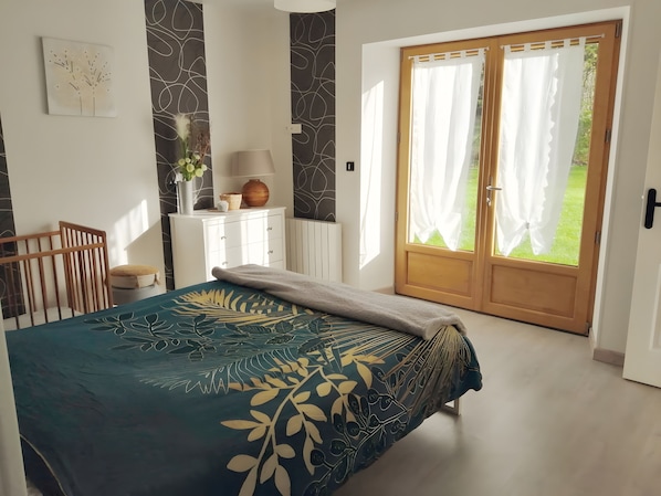 A bedroom with a bed, a dresser, a lamp, and a view of the outdoors.