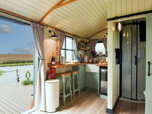 A cozy kitchen with a wooden bar, a view of the sea, and a glass-enclosed shower. - Shepherd Hut at Garden Cottage (Chepstow)