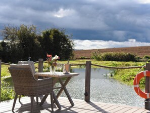 A deck with a table and chairs overlooking a body of water, with a rope barrier and a life buoy. - Shepherd Hut at Garden Cottage (Chepstow)
