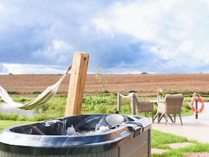 A hot tub outdoors with a hammock, chairs, and a lifebuoy. - Shepherd Hut at Garden Cottage (Chepstow)