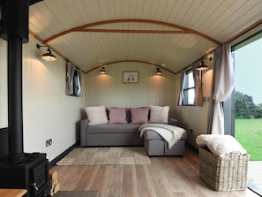 A cozy interior with a sofa, a woven basket, and a black stove. - Shepherd Hut at Garden Cottage (Chepstow)